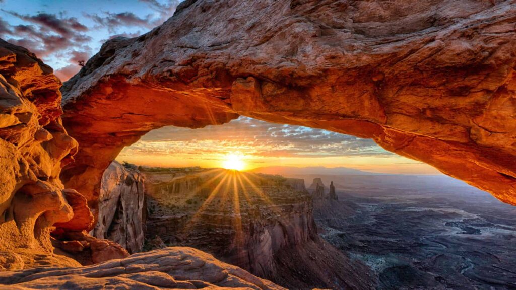 Mesmerizing sunset over Canyonlands National Park, framed by a captivating canyon arch and majestic mesas.